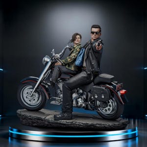 May include: A detailed statue of two figures on a black motorcycle. One figure, wearing sunglasses and a leather jacket, points a gun. The other figure wears a camouflage jacket and a backpack. The motorcycle is black with red accents.