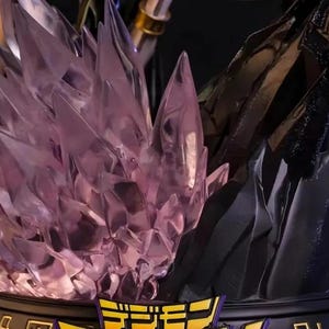 May include: A detailed statue base featuring a central cluster of translucent, purple crystal formations. The base has a black and gold trim with Japanese text. The background is dark, highlighting the statue's intricate design.