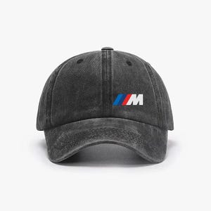 May include: A black, distressed baseball cap featuring the BMW logo in blue, red, and white. The cap has a curved brim and an adjustable strap. The hat is made of a durable fabric.
