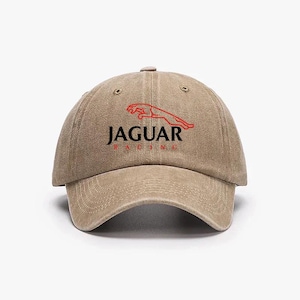 Op de afbeelding: Een beige baseballcap met het Jaguar-logo in rood en zwart. De cap heeft een gebogen klep en een verstelbare band. De tekst "JAGUAR RACING" is op de voorkant gedrukt.
