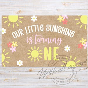 Puede incluir: Un letrero rectangular con fondo marrón presenta el texto "OUR LITTLE SUNSHINE is turning ONE" en blanco y rosa. Ilustraciones de soles y flores amarillas rodean el texto. El letrero también incluye el texto "With all my art" y "Custom Designs".