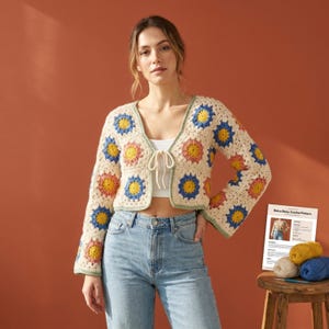 Peut inclure: Cardigan en crochet crème avec des motifs floraux colorés jaunes, bleus et roses. Le cardigan à col en V a une fermeture à nouer et des manches évasées. Le vêtement fait partie d'un modèle de crochet rétro daisy.