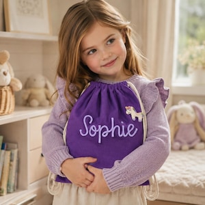 Può includere: Uno zaino a sacca viola con il nome Sophie ricamato in un carattere corsivo viola chiaro. La borsa presenta una piccola toppa ricamata a forma di unicorno sul lato superiore destro ed è dotata di spessi cordini color crema.