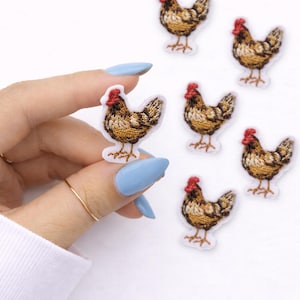 May include: Embroidered patches featuring a detailed hen design. The patches showcase a brown and tan hen with a red comb, set against a white background. Several patches are visible, with one held by a hand with blue nails.