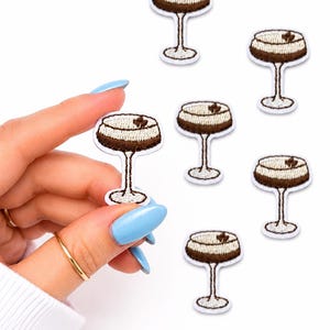 May include: Embroidered patches featuring a cocktail design. Each patch depicts a brown and white cocktail in a stemmed glass. The patches are white with a brown border and are suitable for decorating clothing or accessories.