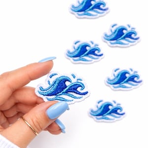 May include: Embroidered patches featuring a blue wave design. The patches have a white border and are in various sizes. The image shows a hand holding one patch, with several others scattered around on a white background.