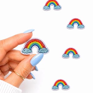 May include: Embroidered rainbow patches with vibrant colors of red, orange, yellow, green, blue, and purple. Each patch features a rainbow arching over two fluffy blue clouds. The patches are small, perfect for decorating clothing or accessories.