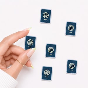 May include: Six small rectangular embroidered patches featuring a dark blue background with a light yellow globe icon and a horizontal line at the bottom, resembling a passport cover. The patches have a light blue border and a textured fabric finish.