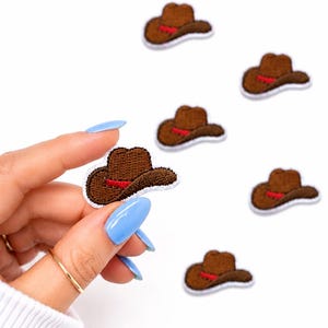 May include: Embroidered brown cowboy hat patches with a red band and white border. One patch is held by a hand with blue nails, and several others are scattered on a white background. These patches are ideal for DIY projects.