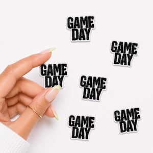 May include: Five individual embroidered patches featuring the text GAME DAY in bold black capital letters. Each patch has a white border and a textured fabric surface, arranged in a scattered pattern against a plain white background.