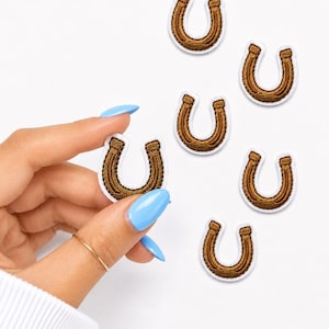 May include: A collection of six small, embroidered horseshoe patches. Each patch features a brown horseshoe shape with a distinct white border. The horseshoe design is rendered in a textured thread pattern, creating a clear, raised appearance.