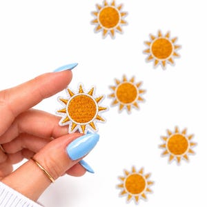 May include: Embroidered sun patches with a yellow center and white and yellow rays. The patches are small and round, with a white border. Several patches are scattered on a white background.