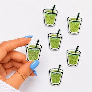 May include: A collection of six embroidered patches, each depicting a small glass filled with a bright green liquid and a dark green straw. The patches feature a white border and are arranged in a cluster on a plain white background.
