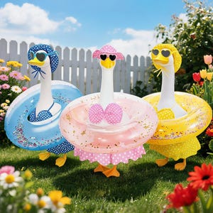 May include: Three whimsical goose figurines in swimsuits and sunglasses, each with a different colored inflatable ring. The geese are on a grassy lawn with a white picket fence and flowers in the background.