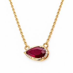 May include: A gold chain necklace featuring a pear-shaped deep red ruby pendant. The ruby is framed by a delicate border of small, clear round-cut diamonds set in gold, suspended from a polished gold cable chain with circular link connectors.