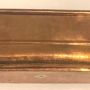 May include: An oblong copper container with a polished, metallic finish and rounded corners. The vessel features a smooth, continuous wall design with a slightly raised rim and a flat base, showcasing the warm, reddish-brown tones of the metal.