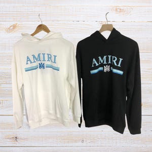 Unisex AMIRI-style hoodies in black and white with bold front graphic and stripe design, pullover streetwear sweatshirts with hood and kangaroo pocket.