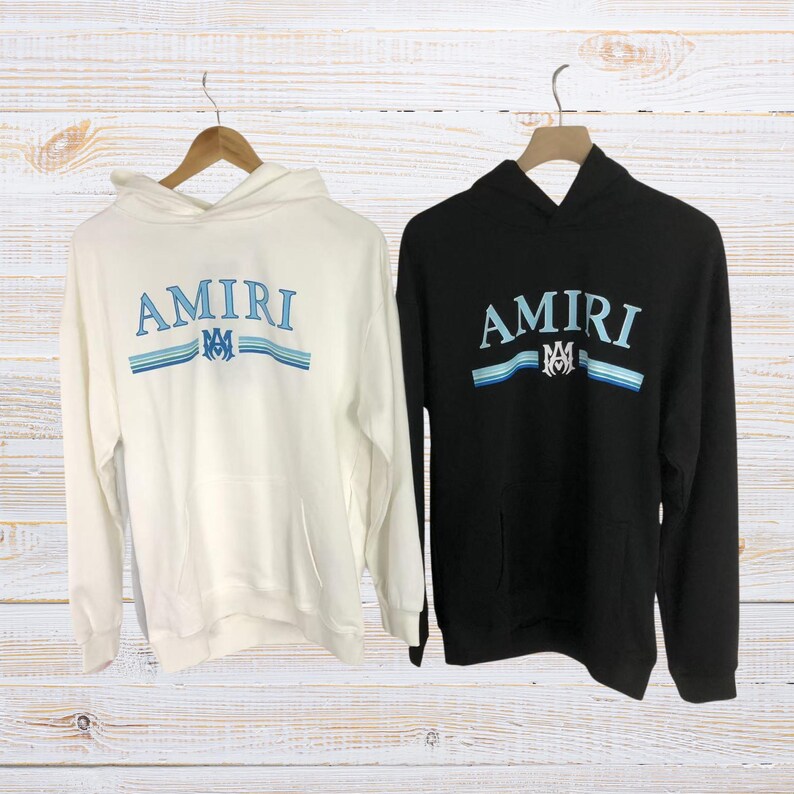 Unisex AMIRI-style hoodies in black and white with bold front graphic and stripe design, pullover streetwear sweatshirts with hood and kangaroo pocket.
