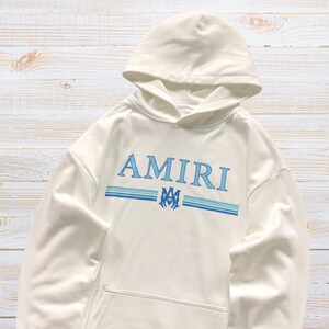 Unisex AMIRI-style hoodies in black and white with bold front graphic and stripe design, pullover streetwear sweatshirts with hood and kangaroo pocket.