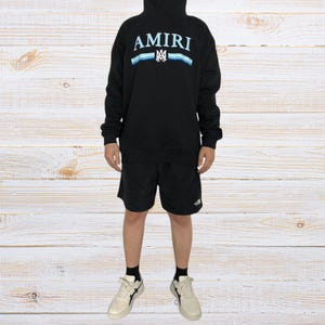 Unisex AMIRI-style hoodies in black and white with bold front graphic and stripe design, pullover streetwear sweatshirts with hood and kangaroo pocket.