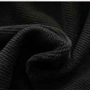 Puede incluir: Primer plano de tela negra con un patr&oacute;n texturizado y tejido. El material est&aacute; doblado, creando sombras y resaltando la profundidad y textura de la tela. El color oscuro sugiere una prenda o textil.