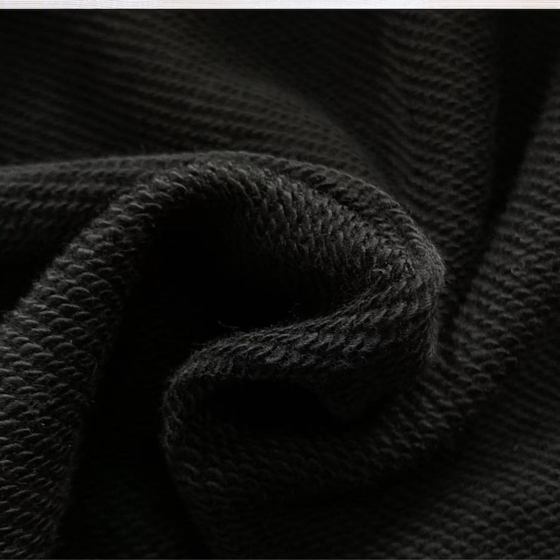 Puede incluir: Primer plano de tela negra con un patr&oacute;n texturizado y tejido. El material est&aacute; doblado, creando sombras y resaltando la profundidad y textura de la tela. El color oscuro sugiere una prenda o textil.