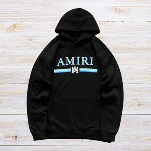 Unisex AMIRI-style hoodies in black and white with bold front graphic and stripe design, pullover streetwear sweatshirts with hood and kangaroo pocket.