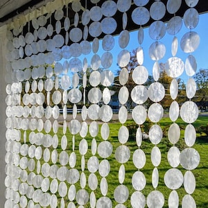 May include: A hanging room divider curtain composed of numerous translucent, circular white capiz shell discs strung together in vertical strands. The discs are arranged in a repeating pattern, creating a shimmering, semi-transparent screen.