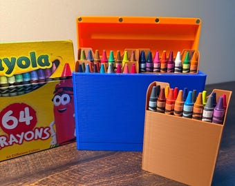 May include: A yellow Crayola 64 crayons box next to a blue plastic storage case with an orange lid containing assorted crayons, and a smaller tan plastic holder filled with upright crayons, all arranged on a dark wooden surface.