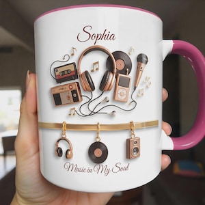 May include: White ceramic mug with a pink interior and handle, featuring musical elements like headphones, a cassette tape, and a vinyl record. The mug is personalized with the name "Sophia" and the phrase "Music in My Soul."