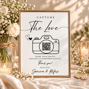May include: A rectangular sign in a gold frame featuring the text CAPTURE The Love, a camera icon with a QR code lens, and the text SHARE YOUR PHOTOS AND HELP US REMEMBER OUR DAY, Thank you!, WITH LOVE, Samira & Rufus, with two small hearts.