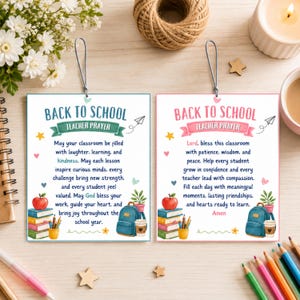 Könnte beinhalten: Zwei rechteckige Hängeanhänger mit abgerundeten Ecken, einer mit türkisfarbenem und einer mit rosa Rand. Beide zeigen den Text BACK TO SCHOOL TEACHER PRAYER, Illustrationen von gestapelten Büchern, einem Apfel, einem Rucksack und einem Kaffee.