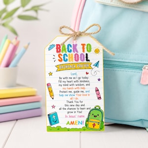 May include: A rectangular white tag with a lined paper background, featuring the text BACK TO SCHOOL BACKPACK PRAYER and a prayer. It is decorated with colorful illustrations of a pencil, crayon, book, and backpack, tied with a brown twine bow.