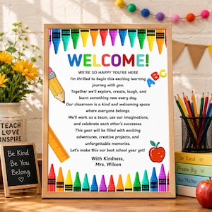 May include: A framed classroom welcome sign with a white background, colorful crayon border, and black text. The sign reads: WELCOME! WE'RE SO HAPPY YOU'RE HERE. I'm thrilled to begin this exciting learning journey with you. With Kindness, Mrs. Wilson.