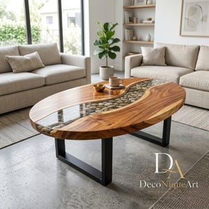 Puede incluir: Una mesa de centro ovalada con un tablero de madera natural que presenta una incrustación central sinuosa rellena de piedras de río lisas y multicolores encapsuladas en resina transparente, sobre dos patas de metal negro en forma de U.