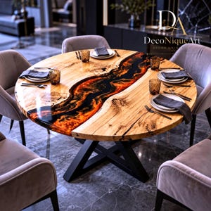 May include: A round dining table with a natural wood grain surface and a central river feature made of black and orange resin. The table has a black metal X-shaped base and is surrounded by four grey upholstered chairs with dark wooden legs.