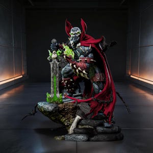 May include: A detailed statue of the comic book character Spawn, featuring a red cape, spiked armor, and a sword with green energy. The figure is posed on a rocky base with a dark, industrial background.