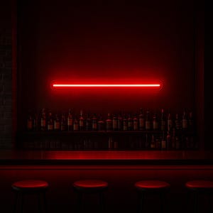 May include: A horizontal, pill-shaped neon light fixture emitting a bright red glow, mounted on a dark wall above a bar counter. The light illuminates a row of glass bottles arranged on a shelf, with four dark stools positioned in the foreground.
