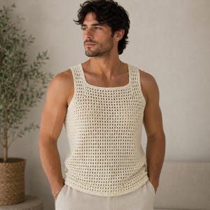 Puede incluir: Una camiseta sin mangas de color crema con un patrón de ganchillo de punto abierto y un escote cuadrado. La prenda está confeccionada con una textura de malla en forma de diamante, consistente y repetitiva en toda la parte frontal, que ofrece un aspecto ligero.