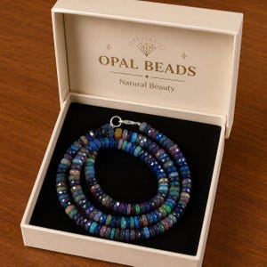 May include: A strand of faceted, multi-colored opal beads in shades of blue, green, and purple, secured with a silver clasp. The necklace is presented in a cream-colored box with the text OPAL BEADS Natural Beauty printed on the lid.