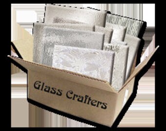 May include: A cardboard box with the words "Glass Crafters" printed on the side. The box is open and contains several pieces of glass, including a clear glass plate, a frosted glass plate, and a patterned glass plate.