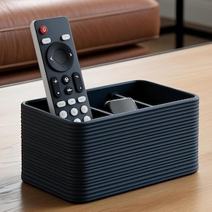 Könnte beinhalten: Ein marineblauer, rechteckiger Fernbedienungs-Organizer mit geripptem Design. Eine schwarze Fernbedienung und ein kleines schwarzes Gerät befinden sich im Inneren des Organizers. Die Fernbedienung hat weiße Tasten und eine rote Ein-/Aus-Taste.