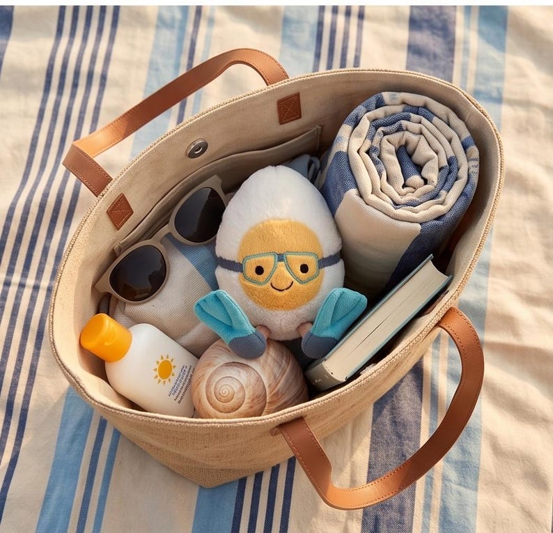 May include: A beige tote bag with brown leather handles, filled with beach essentials. Includes sunglasses, sunscreen, a rolled blue and white striped towel, a book, a seashell, and a plush egg character wearing goggles and flippers.