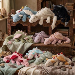 Könnte beinhalten: Eine Sammlung von Plüschdrachen in verschiedenen Farben, darunter Blau, Creme, Schwarz, Grün, Lavendel, Rosa, Bunt und Beige. Jeder Drache besteht aus weichem Stoff, hat Flügel und einen langen Schwanz und ist auf einem Holzregal und Stoff drapiert.