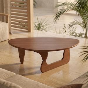 Puede incluir: Una mesa de centro de estilo moderno de mediados de siglo con una superficie lisa de forma ovalada y una base escultural única. La mesa está hecha de madera de tonos cálidos, mostrando la veta natural. El diseño presenta una sola pata de soporte curvada.