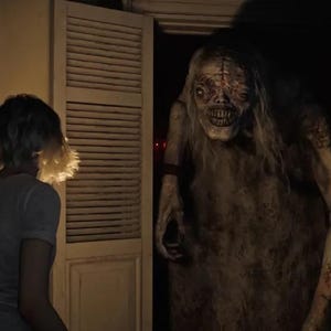 May include: A chilling image of a monstrous figure with long hair and a distorted face in a doorway. A person in a t-shirt is facing the creature. The scene is dark, creating a horror atmosphere.