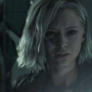 May include: A portrait of a woman with short, grey hair and a worried look. She wears a dark jacket, with a blurred background suggesting an interior. The lighting is subdued, creating a dramatic atmosphere.