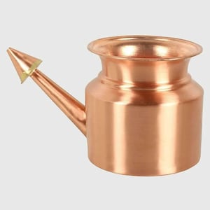 May include: A copper-colored neti pot with a spout and a rounded body. The spout has a conical tip. The pot has a wide opening at the top. The pot is designed for nasal irrigation.