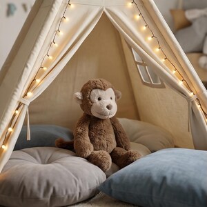 May include: A brown plush monkey sits inside a cream-colored teepee tent decorated with string lights. The monkey is surrounded by gray and blue pillows, creating a cozy and inviting space for children's play or relaxation.