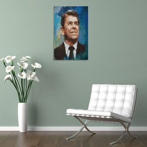 May include: A rectangular wall art print featuring a portrait of Ronald Reagan in a dark suit and tie, rendered in a painterly style with visible brushstrokes against a vibrant blue background, displayed in a room with a white chair and flowers.